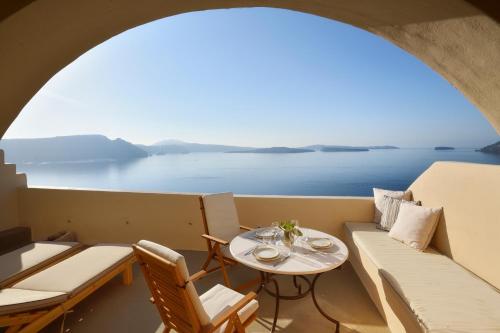 ein Balkon mit einem Tisch und einer Couch und dem Meer in der Unterkunft THE A COLLECTION by K&K in Oia