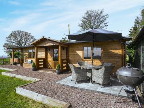 a house with a grill and a table with an umbrella at Stable Lodge At Greenacre in Bromyard