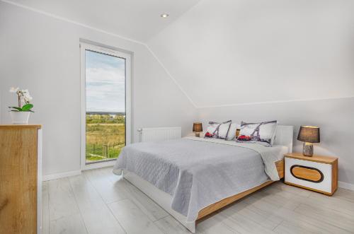 a white bedroom with a bed and a window at Domki apartamentowe Na wrzosach in Jastrzębia Góra