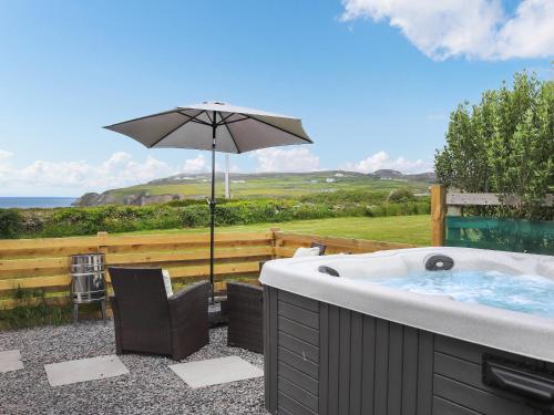 a hot tub with an umbrella and a chair at Uk46570 - Awel Y Mor in Holyhead