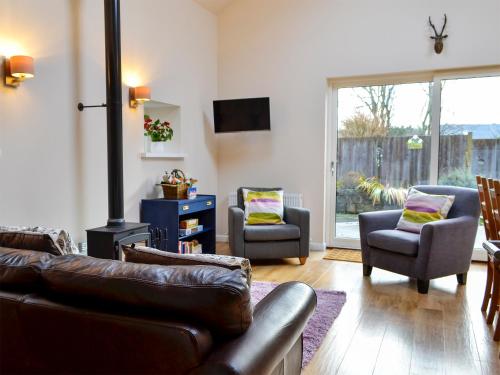a living room with a leather couch and two chairs at Birch Tree Cottage in Edzell