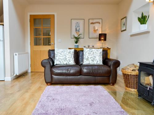 a brown leather couch in a living room with a fireplace at Birch Tree Cottage in Edzell