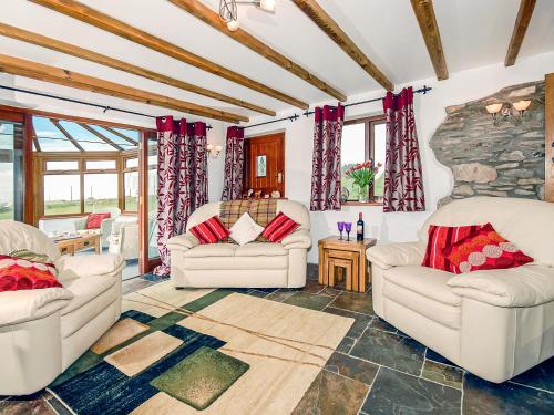 - un salon avec deux chaises blanches et un mur en pierre dans l'établissement Beacon Cottage, à Llanrian