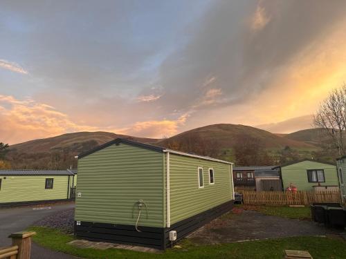 a small green building with mountains in the background at Sheepfold lodge in Sedbergh