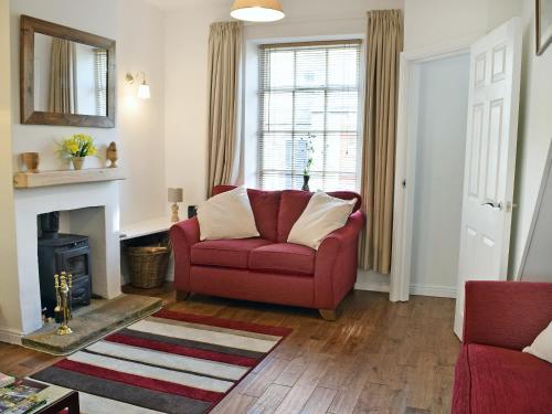 a living room with a red couch and a fireplace at Rose Cottage in Low Bradley