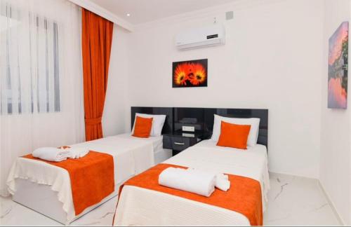 2 camas en una habitación con paredes blancas y almohadas de color naranja en Villa karya, en Kas