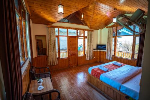 ein Schlafzimmer mit einem Bett und einem Tisch und Fenstern in der Unterkunft The Northwood Cottages Manali, Mountain View with balcony, near mall road, manali in Manali