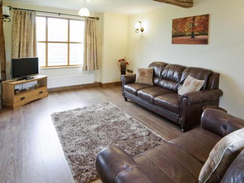 a living room with a leather couch and a television at Cwm Corn Barn - Hw7662 in Mochdre