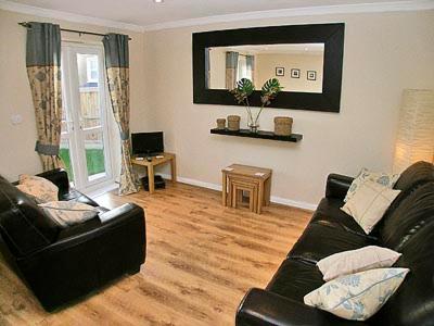 a living room with a black leather couch and a mirror at Breedsmoor Cottage in Ore