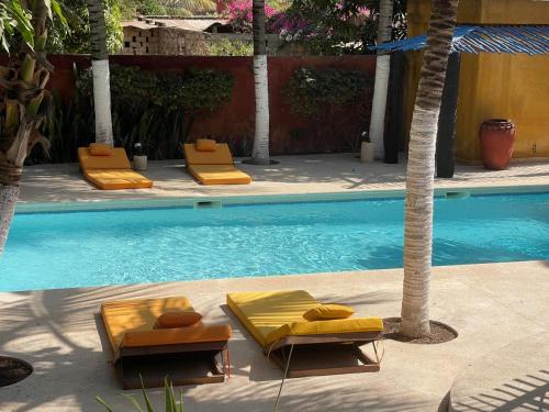 einen Pool mit zwei Liegestühlen neben einer Palme in der Unterkunft La Tour Rouge in M'bour