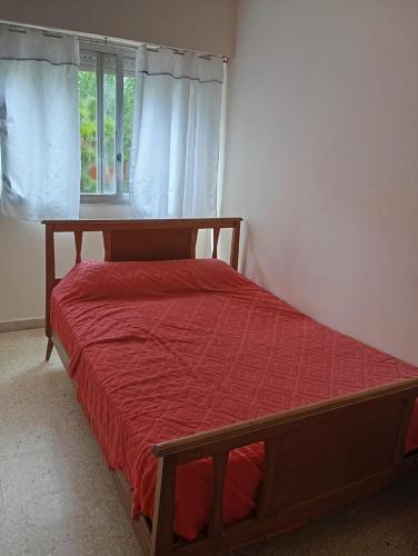 a bedroom with a bed with a red comforter and a window at Departamento San Bernardo - 4 Ambientes - Cochera - Parrilla in San Bernardo