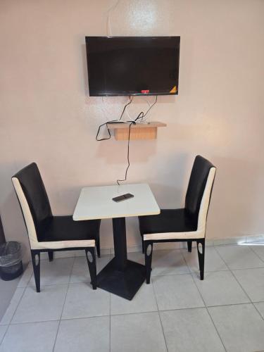 ein weißer Tisch mit zwei Stühlen und einem Fernseher an der Wand in der Unterkunft Shado's residence self catering cotages in Serowe