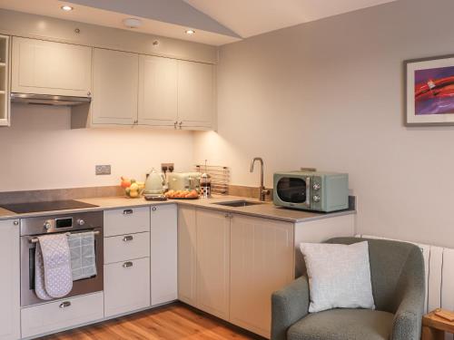 a kitchen with white cabinets and a chair and a microwave at South Snowdon Wharf in Porthmadog