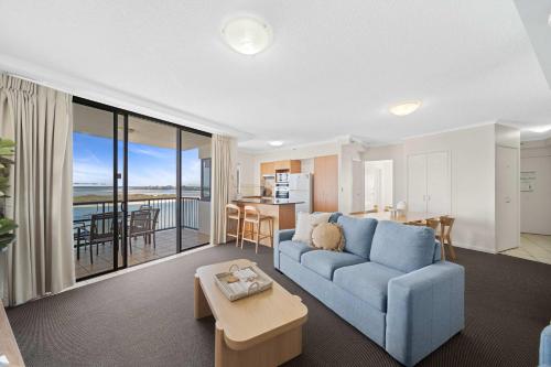 ein Wohnzimmer mit einer blauen Couch und einer Küche in der Unterkunft Seaside Solace at Caloundra Seaview 3BD Apartment in Caloundra