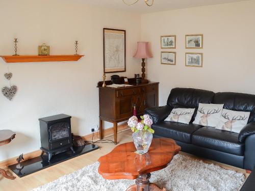a living room with a black leather couch and a wood stove at Seashell Cottage in Nairn