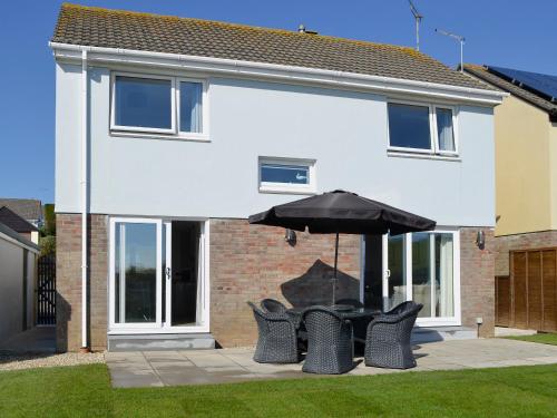 a group of chairs and an umbrella in front of a house at Sand Dunes in Tywardreath