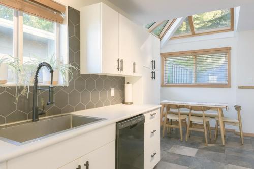 a kitchen with white cabinets and a sink and a table at Tonquin Beach House - EV Charger, Wood Fireplace, Steps from beach in Tofino