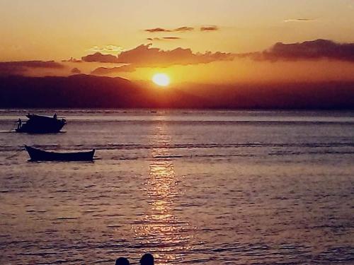 a sunset over the ocean with a boat in the water at Kitinet 06 aconchego, 350 meters from 4 Ilhas in Bombinhas