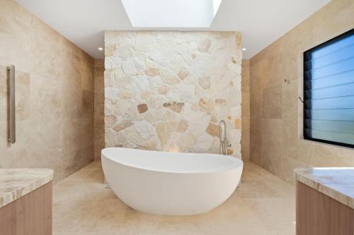 a white tub in a bathroom with a stone wall at Ebony Escape in Casuarina