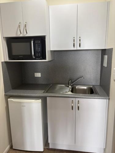 a kitchen with white cabinets and a sink and a microwave at Reef Gardens Motel in Proserpine