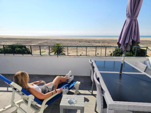 a woman sitting in a chair on a balcony looking at the beach at Panorama Sun Figueira - 1er ligne Mer in Figueira da Foz
