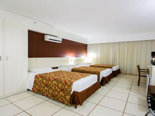 a hotel room with two beds and a television at Apartamento Suites Le Jardin Caldas Novas Goiás in Caldas Novas
