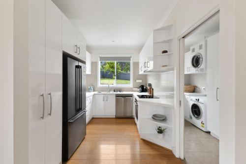 eine weiße Küche mit Spüle sowie Waschmaschine und Trockner in der Unterkunft Lemon & Myrtle Cottage in Myrtleford