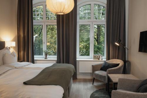 Un dormitorio con una cama y una silla y ventanas. en Home Hotel Norre Park, en Halmstad