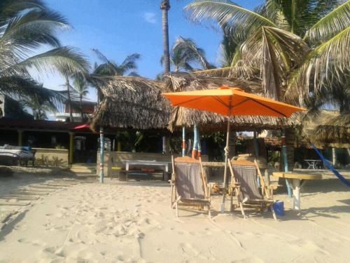 an orange umbrella and chairs on a beach with palm trees at Hotel Gilda in Coyuca