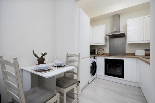 a kitchen with white cabinets and a small table and chairs at Beautiful 1-bed Apartment in Lincoln by Renzo, Lincoln Cathedral, Free Parking! in Lincoln