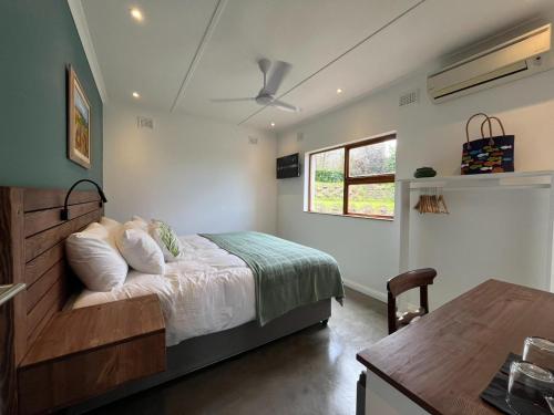 a bedroom with a bed and a window and a table at The Lookout Guesthouse in Uvongo Beach