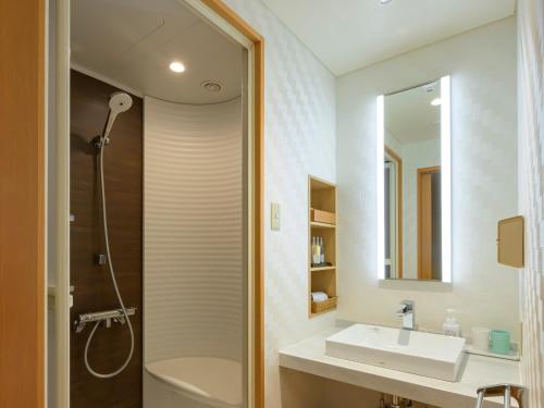 een badkamer met douche, wastafel en spiegel bij Tendo Hotel in Tendo