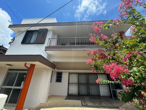 a white house with pink flowers in front of it at 徳之島体験お宿結屋 in Tokunoshima