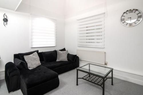 a living room with a black couch and a clock at Bright 3 Bed Ground Floor Flat - Derby in Derby
