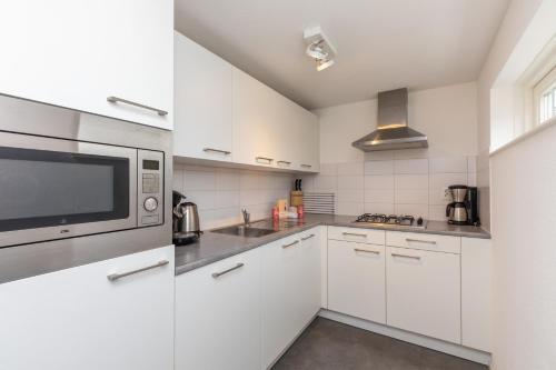 Una cocina con gabinetes blancos y un microondas. en Zonnedorp 26 Renesse: Comfortabele Strandvakantie aan de Noordzee, en Renesse