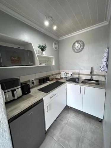 een keuken met witte kasten en een klok aan de muur bij Seebossie in Struisbaai