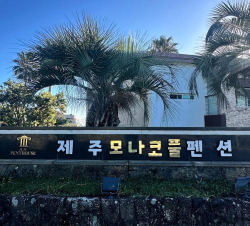 a sign with chinese writing on it next to palm trees at Monaco Pool Pension in Seogwipo