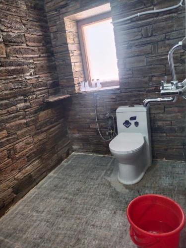a bathroom with a toilet and a window and a red bucket at Pinaka Devbhumi Homestay in Mukteshwar