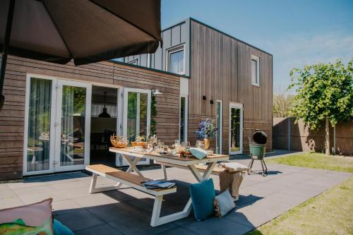 a patio with a table and chairs and a house at Lodge Jacques Cousteau XXL in Renesse