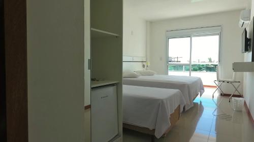 a white bedroom with a bed and a window at Pousada Molhes da Barra in Torres