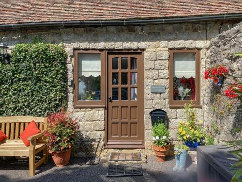 a stone house with a door and a bench and flowers at Stone Hill Oast Annexe in Egerton