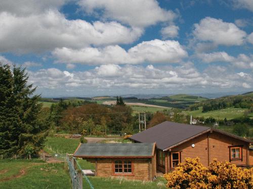 a wooden house in a field with a fence at Bracken Log Cabin - S4468 in Glenfarg