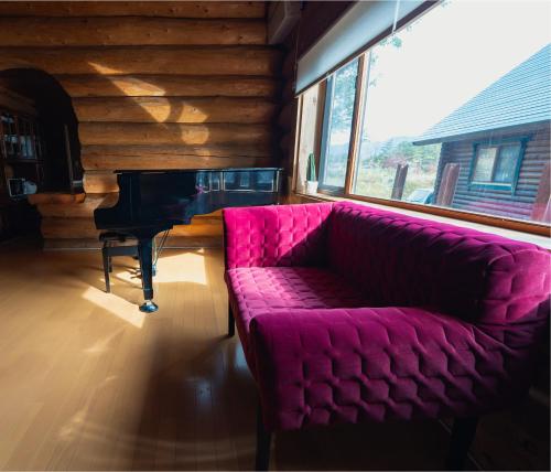 a pink couch in a room with a piano at Hakuba Riverside Loghouse in Hakuba