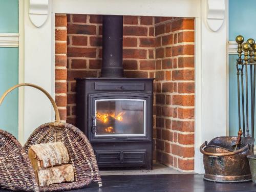 a wood stove in a brick fireplace with two chairs at Hemblington Hall Arts And Leisure Ltd in South Walsham