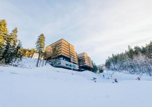 别拉什尼察Wellness Apartments Nomad的一座建在积雪覆盖的山坡上的建筑物，周围有树木。