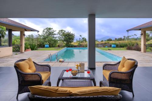 a swimming pool with two chairs and a table in a yard at SaffronStays Maitri in Igatpuri