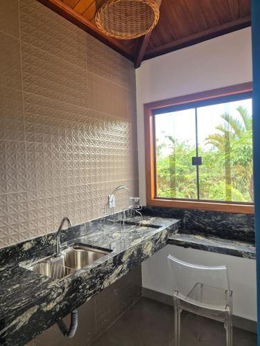 a kitchen with a sink and a window and a chair at Ecopousada Serra Verde in Glaura