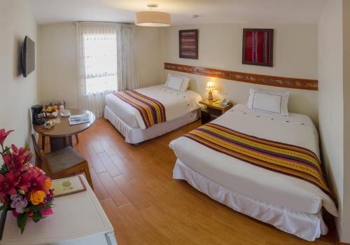 a hotel room with two beds and a table with flowers at Taypikala Hotel Cusco in Cusco