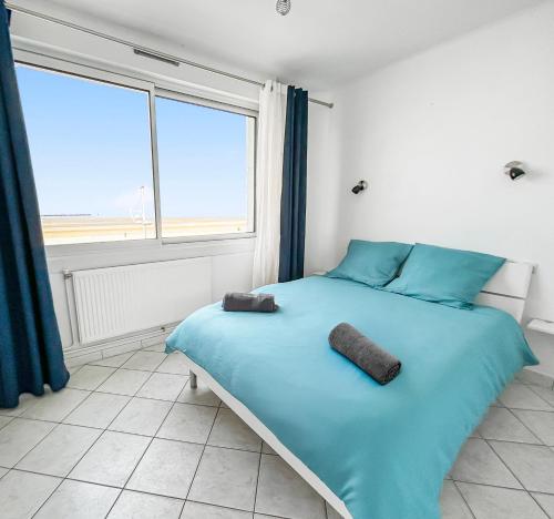 a bedroom with a bed with blue sheets and a large window at Vue panoramique sur la plage, grand T2 in Dunkerque