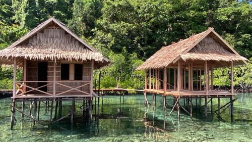 two huts on stilts in a body of water at Batanta Guest House in Pulau Birie